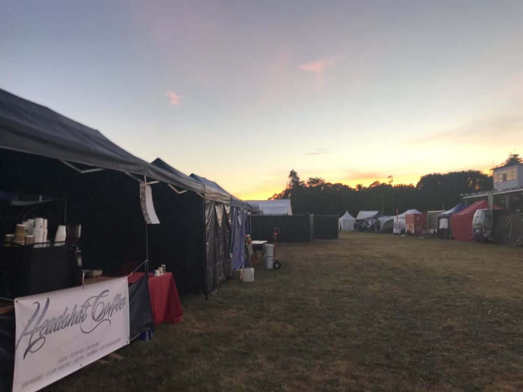 Empty tents and a Headshot Coffee banner on the grass at dusk