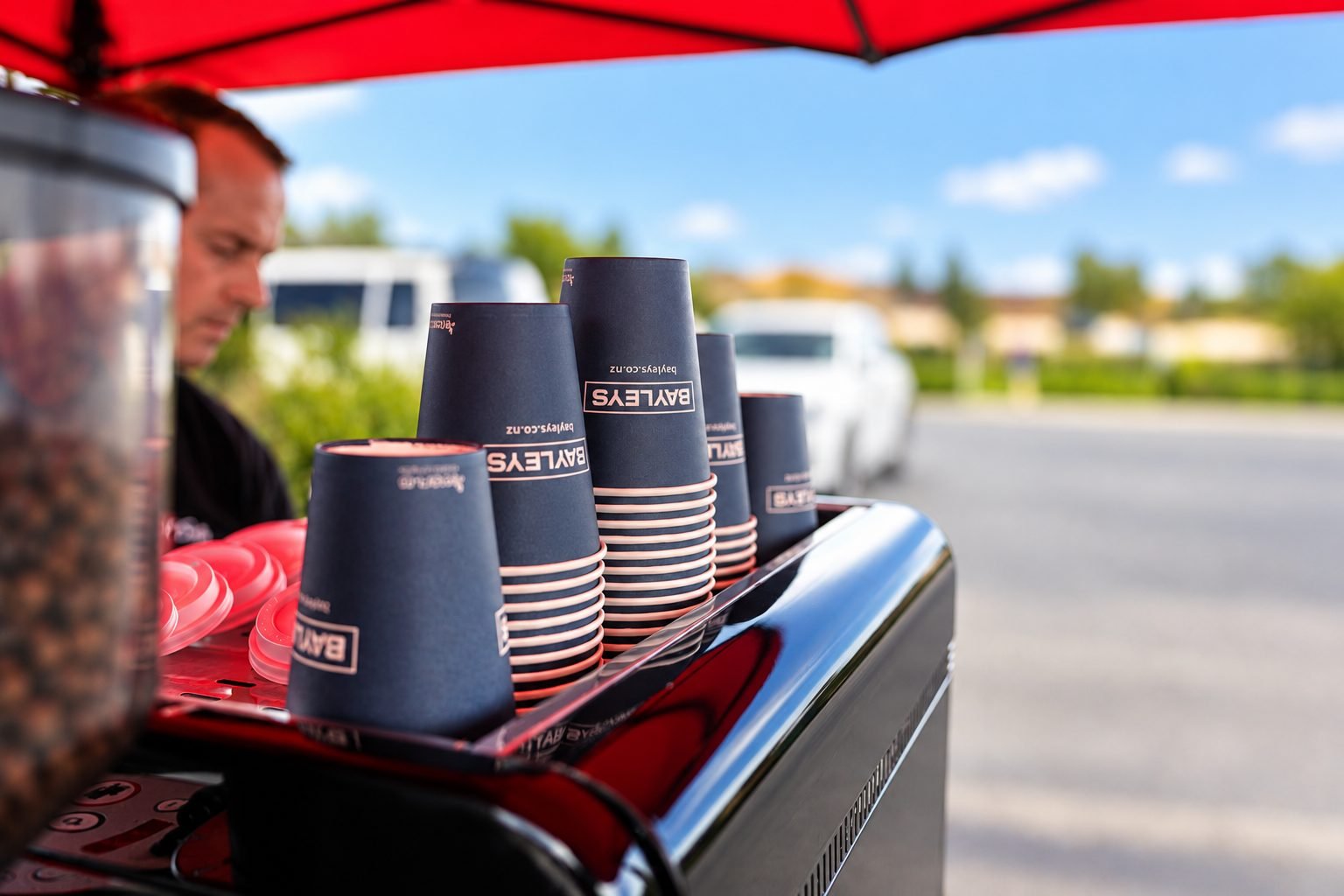 Branded takeaway cups stacked on a red espresso machine